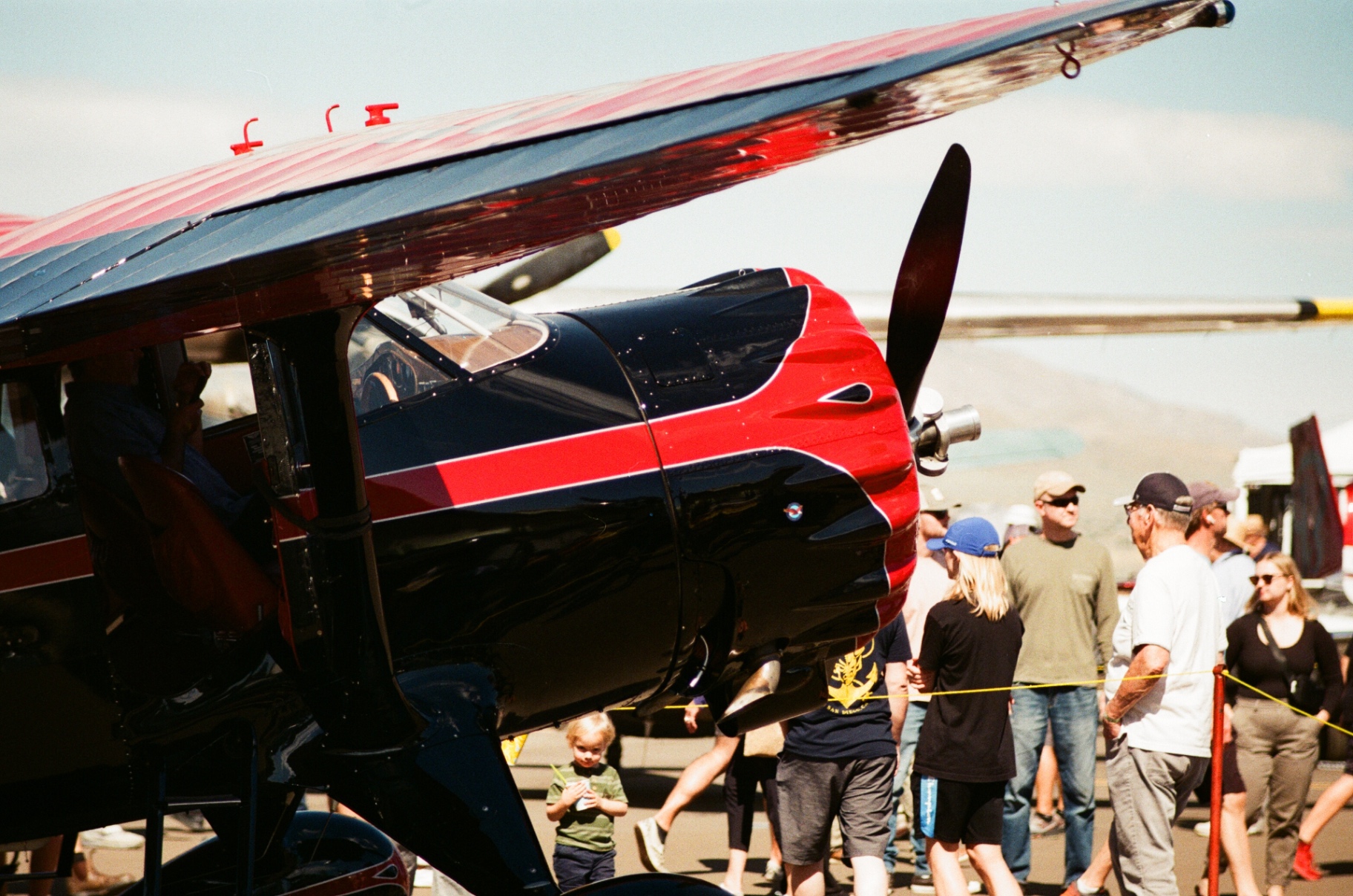 Black and red vintage high-wing aircraft on the airshow ramp with a crowd