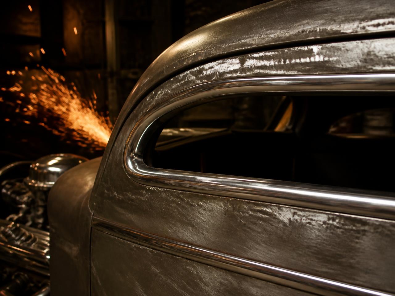 Hand-formed steel bodywork and chrome trim on a custom hot rod in the workshop